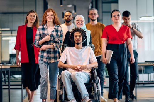 A diverse group of young business people walking a corridor in the glass-enclosed office of a modern startup, including a person in a wheelchair and a woman wearing a hijab.