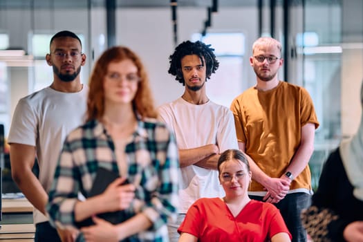 A diverse group of young business people walking a corridor in the glass-enclosed office of a modern startup, including a person in a wheelchair and a woman wearing a hijab.