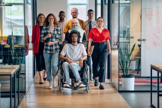 A diverse group of young business people congregates within a modern startup's glass-enclosed office, featuring inclusivity with a person in a wheelchair, an African American young man, and a hijab muslim woman