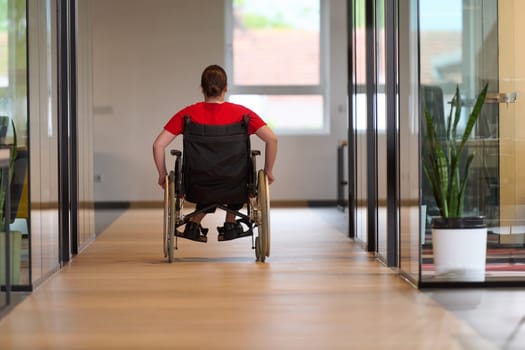 A modern young businesswoman in a wheelchair is surrounded by an inclusive workspace with glass-walled offices, embodying determination and innovation in the business world.