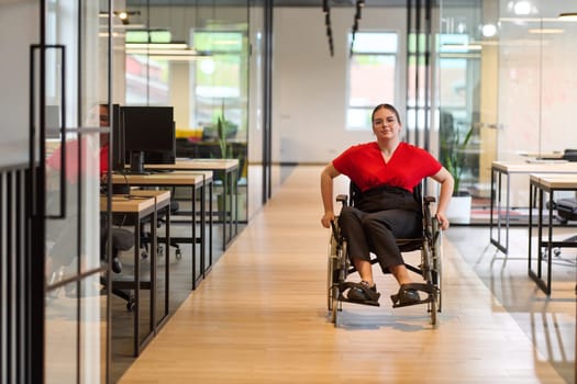 A modern young businesswoman in a wheelchair is surrounded by an inclusive workspace with glass-walled offices, embodying determination and innovation in the business world.