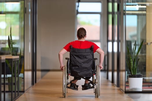 A modern young businesswoman in a wheelchair is surrounded by an inclusive workspace with glass-walled offices, embodying determination and innovation in the business world.