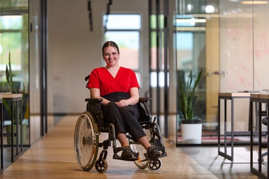 A modern young businesswoman in a wheelchair is surrounded by an inclusive workspace with glass-walled offices, embodying determination and innovation in the business world.