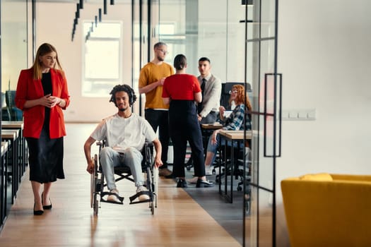 A diverse group of young professionals, including businesswomen and an African-American entrepreneur in a wheelchair, engage in collaborative discussion on various business projects in a modern startup office setting