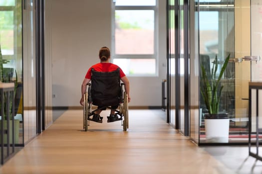 A modern young businesswoman in a wheelchair is surrounded by an inclusive workspace with glass-walled offices, embodying determination and innovation in the business world.