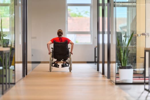 A modern young businesswoman in a wheelchair is surrounded by an inclusive workspace with glass-walled offices, embodying determination and innovation in the business world.