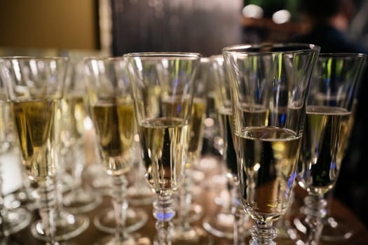 A row of wine glasses are lined up on a table. The glasses are all filled with a clear liquid, and they are all the same size