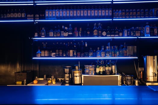 A bar with a blue counter and shelves of liquor. The bar is empty and the lights are on