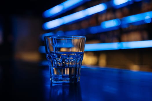 A glass of water sits on a bar counter. The bar is dimly lit, giving the scene a cozy and intimate atmosphere