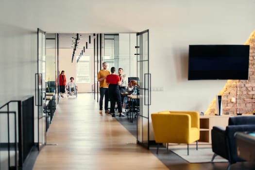 A diverse group of young professionals, including businesswomen and an African-American entrepreneur in a wheelchair, engage in collaborative discussion on various business projects in a modern startup office setting