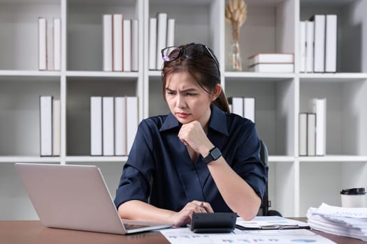 Tired businesswoman wearing glasses has a headache at work looking at a laptop computer in the office.