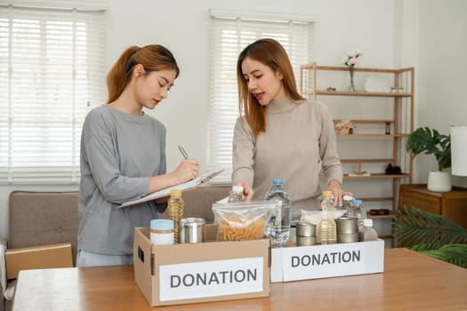 Two young female volunteers help pack food into donation boxes and prepare to donate them to charity.