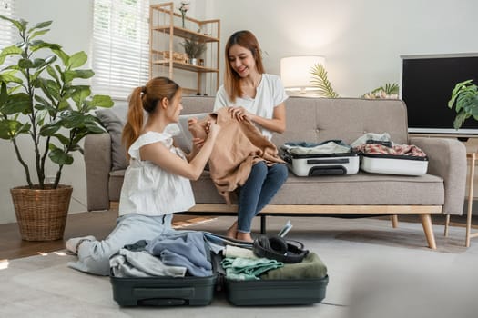 Two young female friends pack their suitcases and clothes to get ready for a weekend together on the living room sofa..