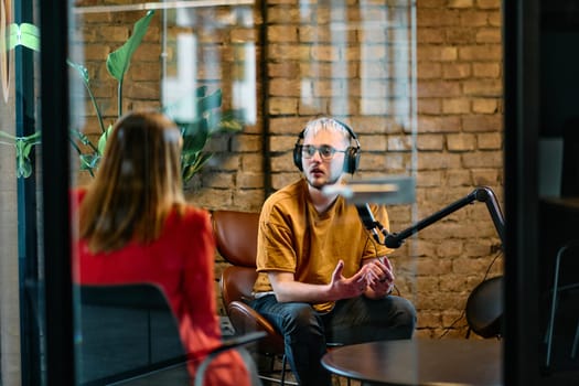 A gathering of young business professionals, some seated in a glass-walled office, engage in a lively conversation and record an online podcast, embodying modern collaboration and dynamic interaction.