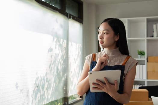 A small SME business owner receives product orders and writes shipping information on tablet in the home office to prepare for delivery..