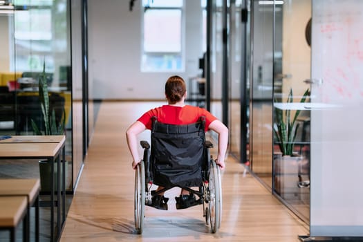 A modern young businesswoman in a wheelchair is surrounded by an inclusive workspace with glass-walled offices, embodying determination and innovation in the business world.