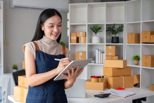 A small SME business owner receives product orders and writes shipping information on cardboard boxes in the home office to prepare for delivery..