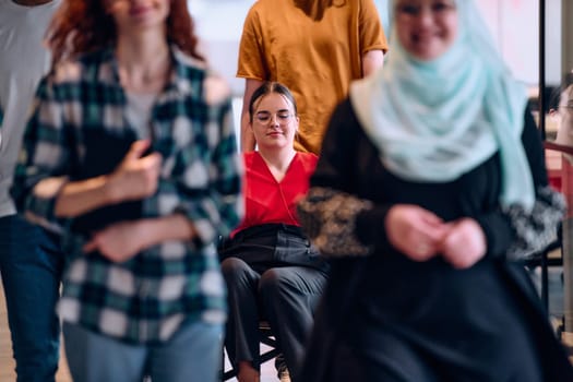 people walking a corridor in the glass-enclosed office of a modern startup, including a person in a wheelchair and a woman wearing a hijab.