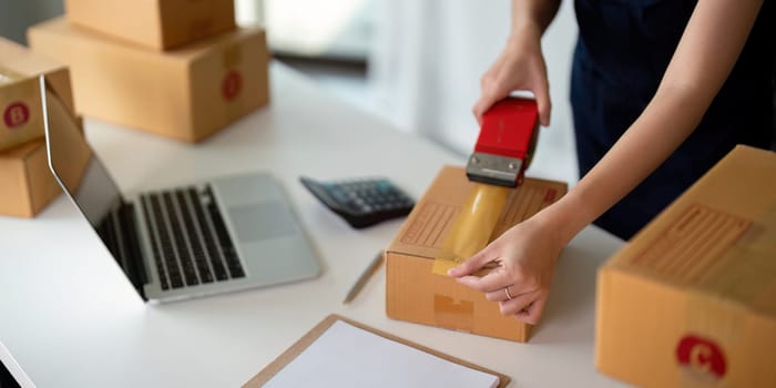 Woman use scotch tape to attach parcel boxes to prepare goods for the process of packaging at home, shipping, online sale internet marketing ecommerce concept startup business idea.