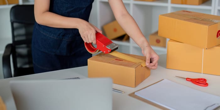 Woman use scotch tape to attach parcel boxes to prepare goods for the process of packaging at home, shipping, online sale internet marketing ecommerce concept startup business idea.