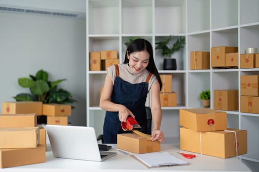 Woman asian use scotch tape to attach parcel boxes to prepare goods for the process of packaging, shipping, online sale internet marketing ecommerce concept startup business idea.