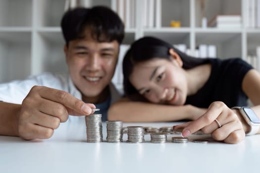 A man and woman are sitting at a table with a pile of coins in front of them. The man is holding a coin and the woman is looking at him. Scene is happy and playful