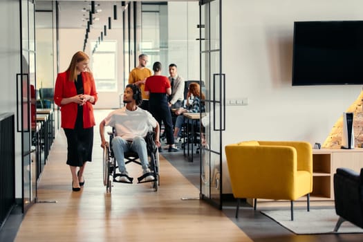 A diverse group of young professionals, including businesswomen and an African-American entrepreneur in a wheelchair, engage in collaborative discussion on various business projects in a modern startup office setting