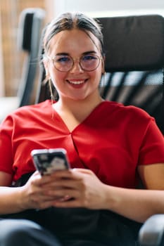 A businesswoman resting on a short break from work in a modern startup coworking center, using her smartphone to unwind and recharge.