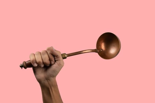 Black male hand holding a brass vintage kitchen ladle isolated on pink background. High quality photo