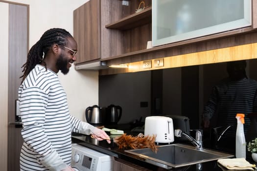 African American man young use duster cleaning in kitchen at home.