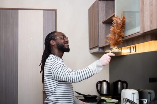 African American man young use duster cleaning in kitchen at home.