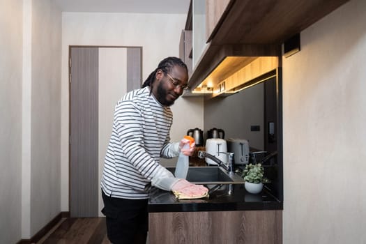 African American man in rubber gloves wipe dust from table in kitchen, Housework, cleaning, lifestyle, household.