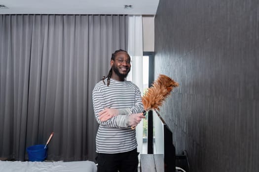 Young African American man for cleaning apartment, holding mop and other cleaning tools. Cheerful african american man housekeeping on weekend.