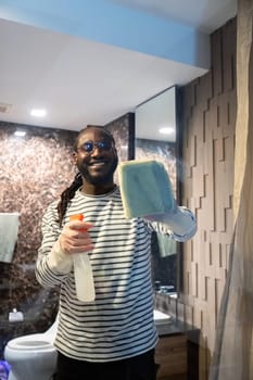 Happy young African American man cleaning the glass in the apartment. Cleaning maintain cleanliness in with towel and spray detergent.