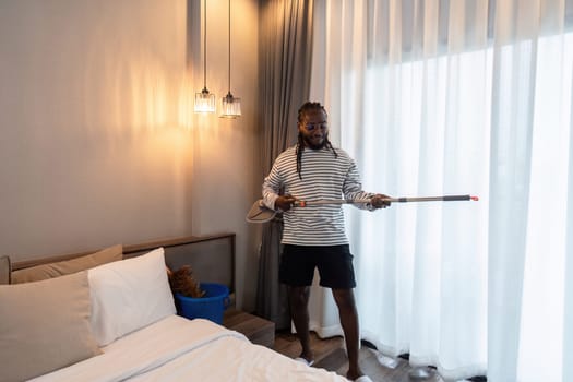 African American man young wipe the floor with a mop while singing in the room at home.