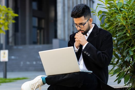 Displeased worried Indian businessman use laptop notebook typing browsing working loses bad news loss database fail computer virus error problem outdoor. Arabian Hindu freelancer executive manager ceo