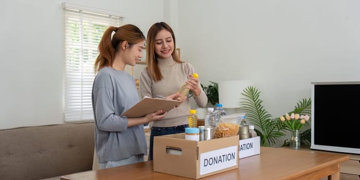 Donation and two woman volunteer asian of happy packing food in box at home. Charity.