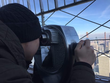 Closeup on a man, boy who is looking through the telescope at manhattan from Empire State Building in winter. High quality photo