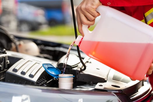 Service worker man pours into car hood engine room windscreen red cleaning washer liquid automobile glass cleaner from canister bottle. Windshield fluid water into windshield washer tank reservoir