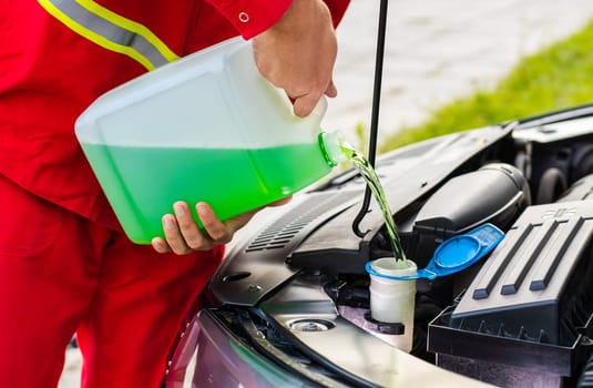 Close-up service worker man driver pouring green non freezing windshield cleaning glass washer fluid into car tank from canister bottle. Summer or winter fluid windscreen liquid glass window cleaner