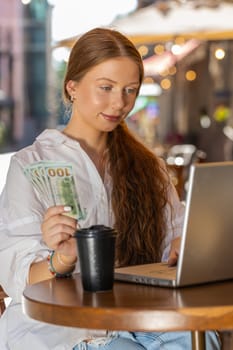 Happy rich freelancer girl counting money dollar cash, use calculator app plans to order gifts food delivery online booking hotel room outdoors. Woman tourist sits at table in city cafeteria. Vertical