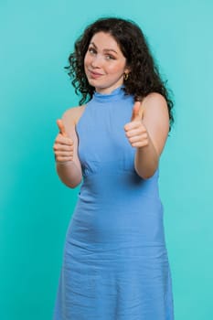 Like. Young woman raises thumbs up agrees with something or gives positive reply recommends advertisement likes good idea. Attractive brunette girl isolated alone on blue studio background. Vertical
