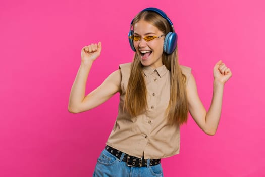 Happy woman in headphones listening music and dancing disco fooling around having fun expressive gesticulating hands relaxing on party. Blonde girl in sunglasses isolated on studio pink background