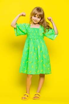 I am strong and healthy. Young girl showing biceps and looking confident feeling power strength to fight for rights, energy to gain success win. Preteen blonde child kid on yellow background. Vertical
