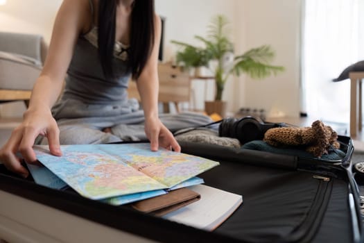 Asian woman packing suitcase or luggage and planning to travel on summer vacation on map.