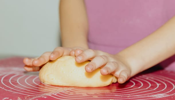 One unrecognizable Caucasian girl stands at the table and kneads yellow shortbread dough with her hands on a pink silicone mat, close-up side view. Step by step instructions. Step 9