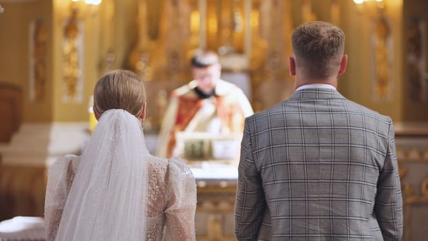 A bride and groom stand back to back in a Catholic church during their wedding