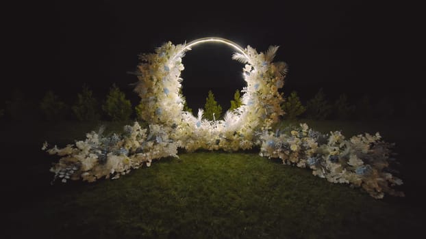 White flowers arch at the wedding ceremony. Outdoors decoration. Romantic rustic style. Lamps lights in the evening.