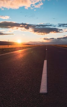 Empty intercity countryside asphalt road with the blue sky, sun and clouds on the background at sunset. Beautiful landscape