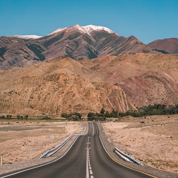 Empty asphalt road in front of huge majestic mountains with snow covered peaks. Beautiful landscape of Altay region, Russia.